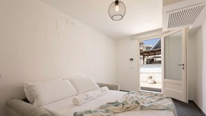 Une chambre d’hôtel comprenant un lit, une chaise, un luminaire suspendu et une porte donnant sur un espace extérieur.