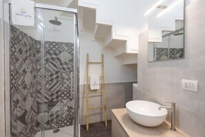 A modern bathroom with a geometric patterned shower wall, a white sink, a mirror, and a wooden ladder.