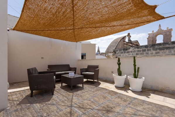 A rooftop patio with wicker furniture, potted cacti, and a view of historic architecture.