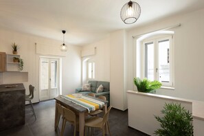 A modern kitchen with a dining area, a sofa, and a window with plants.
