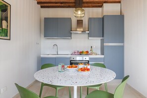 A kitchen with blue cabinets, a white countertop, a round table with green chairs, and a hanging light fixture.