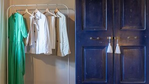 A clothing rack with various garments, a blue wardrobe with brass handles, and a white wall.