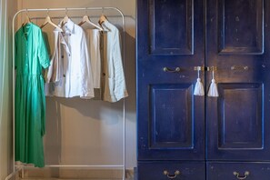 Un perchero con varias prendas de vestir, un armario azul con tiradores de latón y una pared blanca.