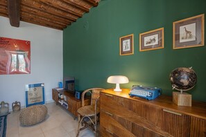 Una habitación con un escritorio de madera, un globo terráqueo, cuadros enmarcados, una silla de mimbre y una lámpara.