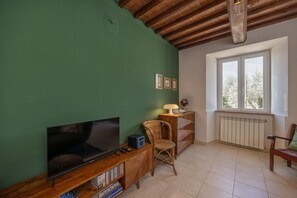 Una sala de estar con televisión, una silla de mimbre, estantes de madera y una ventana con vistas.