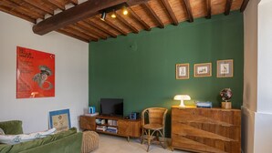 A living room with a green wall, wooden ceiling beams, a sofa, a TV stand with books, and framed pictures.