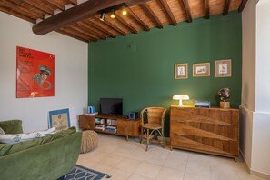 Una sala de estar con pared verde, vigas de madera en el techo, un sofá, un mueble de televisión con libros y cuadros enmarcados.