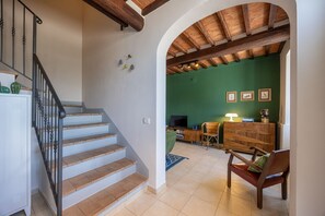 Una escalera conduce a un espacio de estar con un muro verde, mobiliario de madera y un televisor.