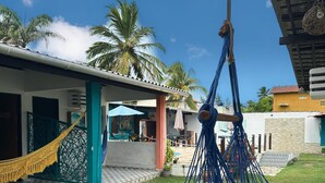 Un hamac bleu est suspendu à l’extérieur, avec un bâtiment et des palmiers en arrière-plan.