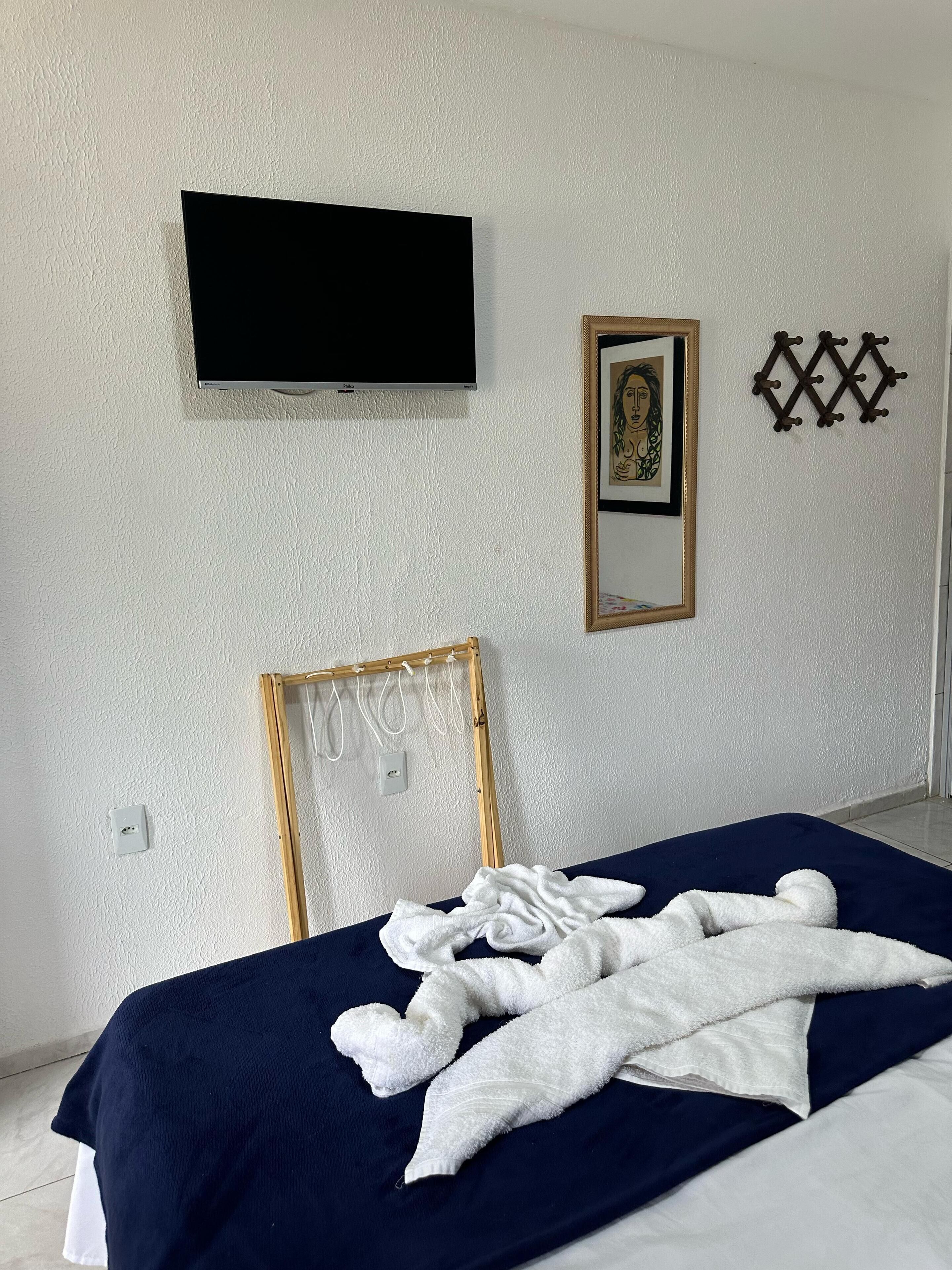 A bedroom with a bed, a television mounted on the wall, a framed picture, and a decorative wall piece.