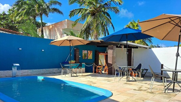 Une piscine entourée de palmiers et d’un mur bleu, avec des chaises longues et des parasols.
