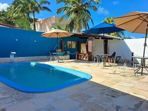 Une piscine entourée de palmiers et d’un mur bleu, avec des chaises longues et des parasols.