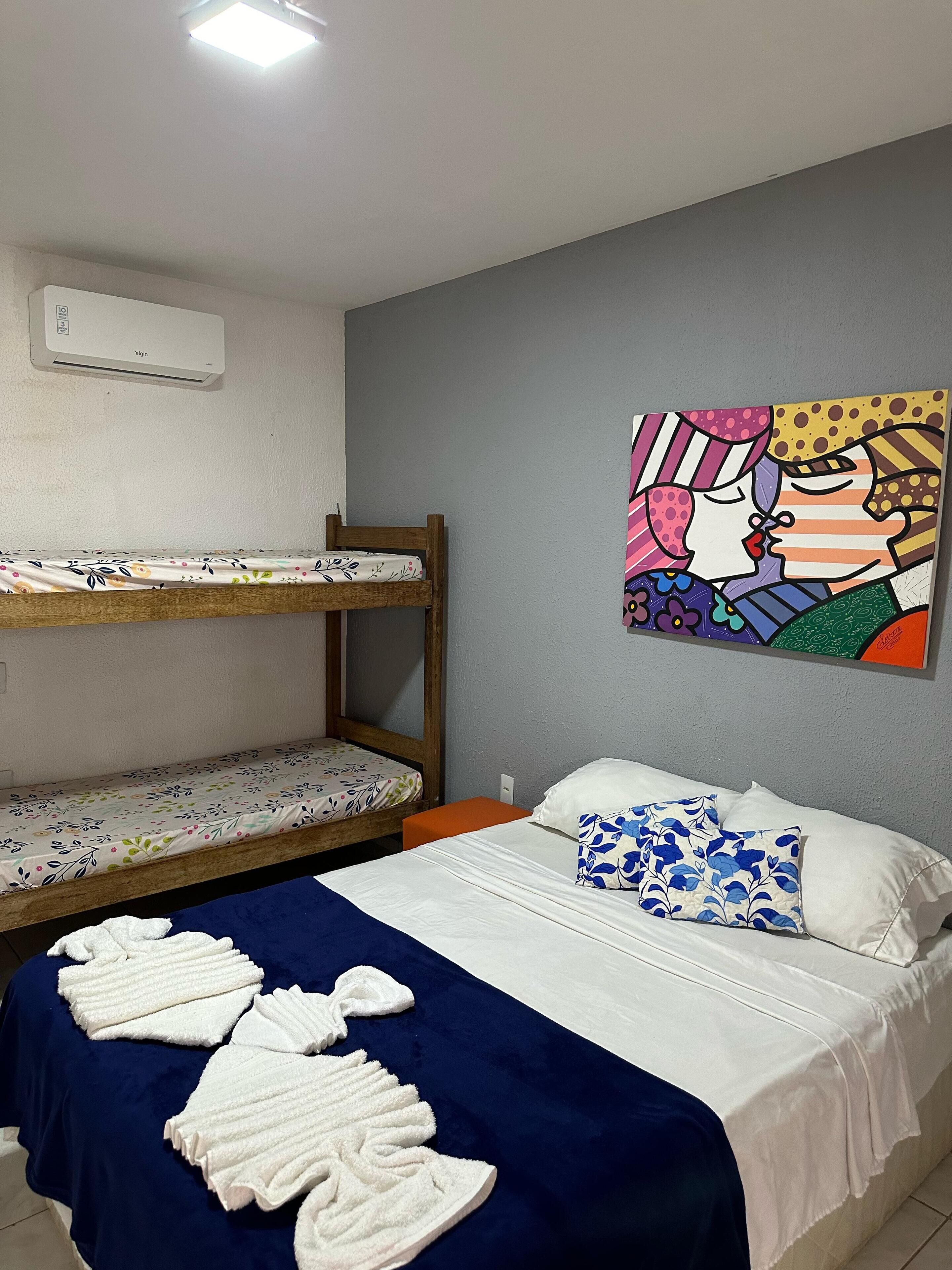 A room with bunk beds, a bed with a blue blanket, white pillows, and a colorful painting on the wall.
