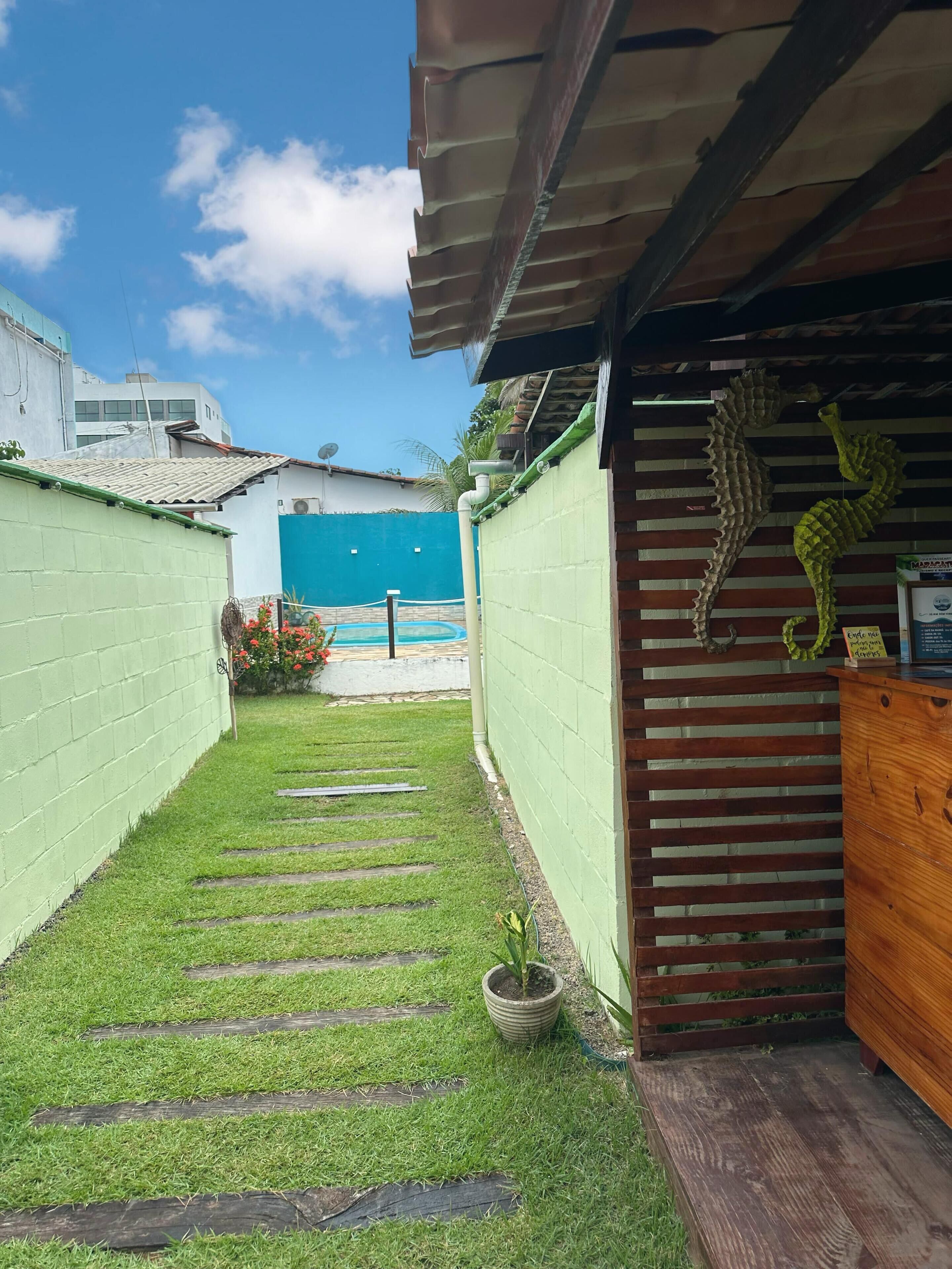 Un sendero estrecho con tablones de madera que conduce a un muro verde con una estructura de madera decorada con una escultura de caballito de mar.