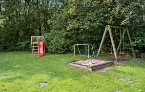 Un parque infantil con un tobogán, columpios y un arenero.