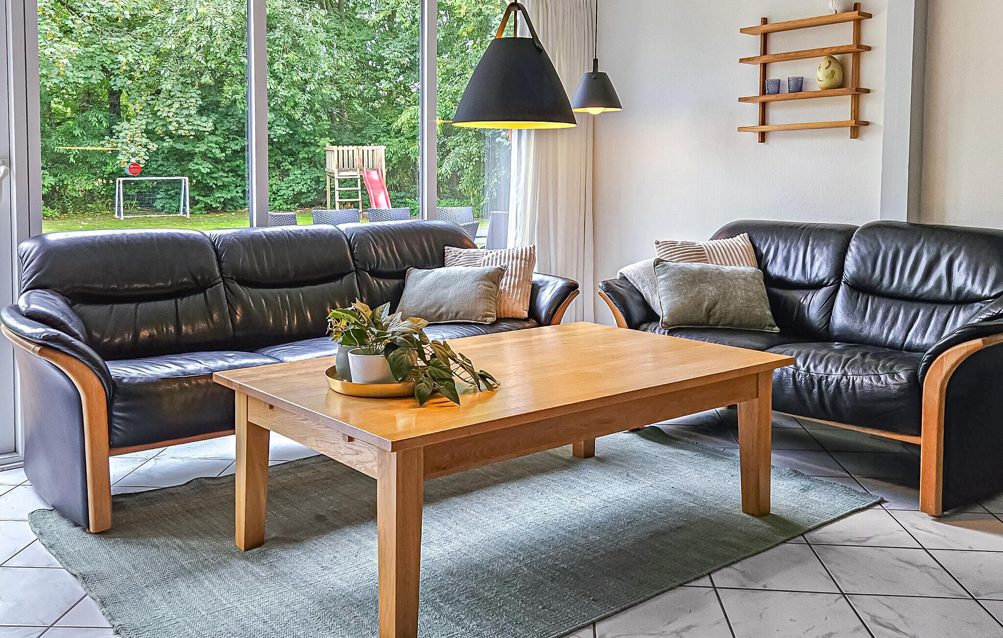 Ein Wohnzimmer mit zwei schwarzen Ledersofas, einem Holztisch und einem großen Fenster mit Blick auf Grünflächen.