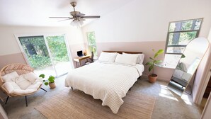 A bedroom with a bed, a chair, a desk, a potted plant, and a ceiling fan.