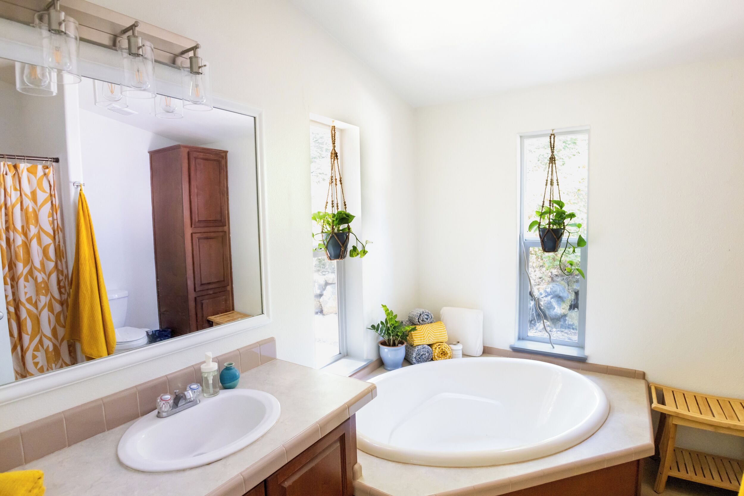 A bathroom with a large bathtub, a double sink, a mirror, and two hanging plants.