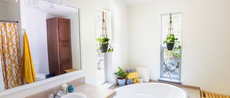 A bathroom with a large bathtub, a double sink, a mirror, and two hanging plants.