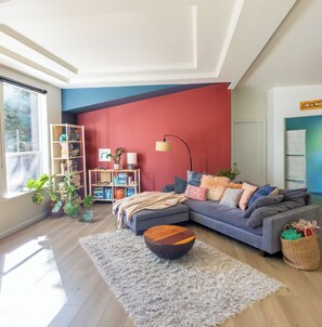 Un salon moderne avec un canapé d’angle, une table basse en bois, une bibliothèque et une grande fenêtre.