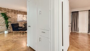 A room with a brick wall, a white door, a black chair, a potted plant, and a large window with curtains. - Walkable Dtwn 2B Getaway | Sleeps 6 | Pool, Prkg (Austin)