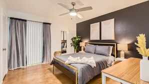 A modern bedroom with a bed, bedside tables, a ceiling fan, and a view of the outdoors through a window with curtains. - Walkable Dtwn 2B Getaway | Sleeps 6 | Pool, Prkg (Austin)