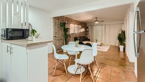 A compact kitchen with white cabinets, a black microwave, and a dining area with white chairs and a round table. - Walkable Dtwn 2B Getaway | Sleeps 6 | Pool, Prkg (Austin)