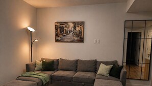 Ein Wohnzimmer mit einem Ecksofa, einem runden Couchtisch, einer Stehlampe und einem Gemälde an der Wand.