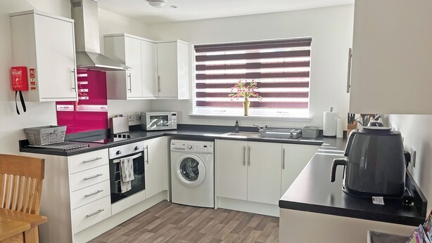 A modern kitchen with white cabinets, a microwave, a washing machine, and a kettle.