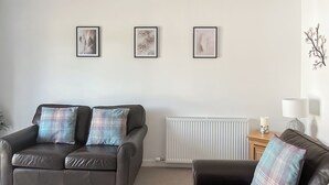 A living room with two black leather sofas, each with plaid cushions, a white radiator, and three framed wall art pieces.
