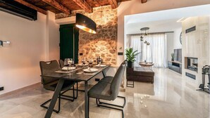 A dining area with a stone wall, wooden ceiling beams, and modern furniture. - Luxurious home in Poljaci (Poljaci)