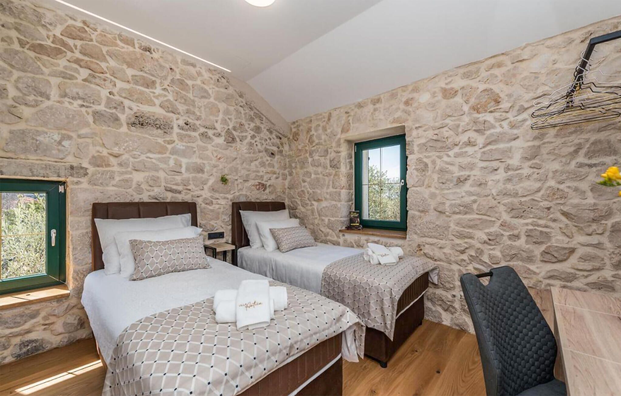 A room with two beds, stone walls, a window, and a chair.