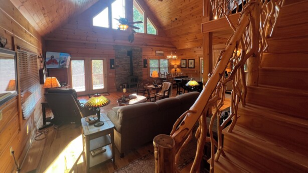 A cozy log cabin interior with a fireplace, wooden furniture, and a staircase.