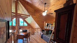A cozy cabin with a loft bedroom, wooden floors, a dining area, and a ceiling fan.
