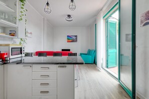 Een moderne keuken met een centraal eiland, witte kasten en een eethoek met een rode bank en turquoise kussens.