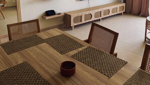 Un moderno salón con una mesa de comedor de madera, individuales tejidos y un televisor montado en la pared.