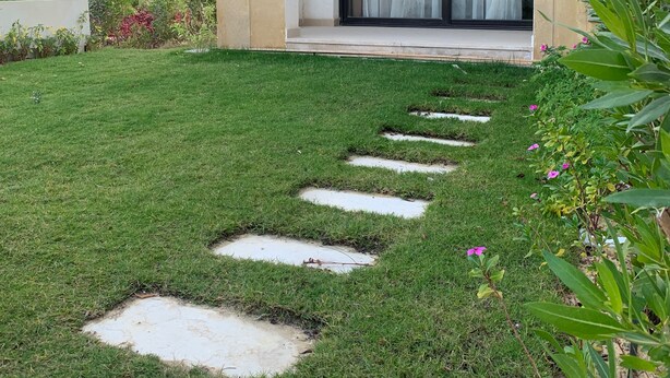 Un edificio moderno con techo plano, un ventanal con cortina y un pequeño jardín con piedras para caminar.