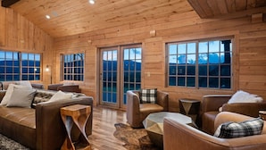 A log cabin interior with a cozy seating area, large windows, and a wooden ceiling. - EML 7 Cloven-Hoofed (Paonia)