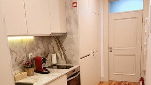 A compact kitchen with a marble countertop, a built-in oven, and a small sink. There is a red coffee machine and a basket with flowers on the counter. A door with a fire extinguisher is visible in the background. - Premium Apartment Porto Downtown, With Terrace (Porto)