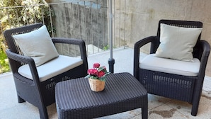 A patio area with two wicker chairs and a matching table, each with a cushion. A small basket with flowers is placed on the table. - Premium Apartment Porto Downtown, With Terrace (Porto)