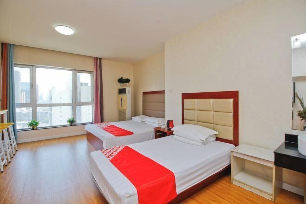 A hotel room with two beds, a desk, a chair, and a window with a city view.