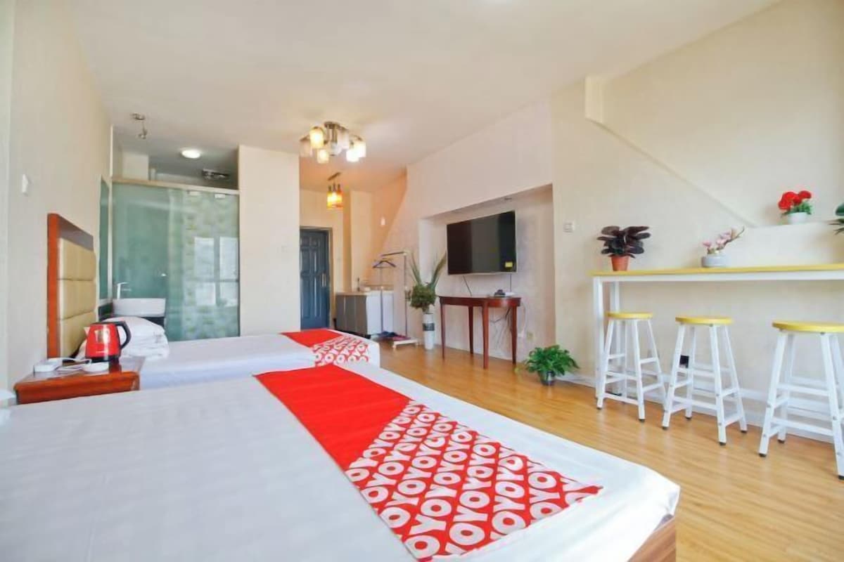 A hotel room with a large bed, a desk with a chair, a TV, and a small kitchen area.