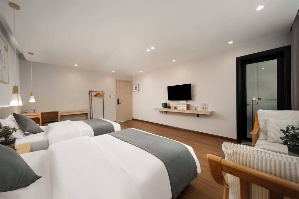 A modern hotel room with two beds, a TV, a chair, and a small table.