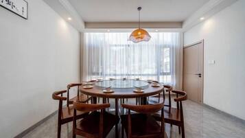 A round dining table with six chairs, a hanging pendant light, and a door in the background.