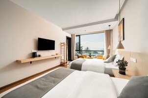 Habitación de hotel con cama, televisor, ventana con vistas y una mesita con una planta.