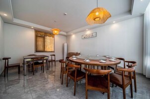 A dining area with a round table, wooden chairs, a hanging light fixture, and a window with a decorative screen.