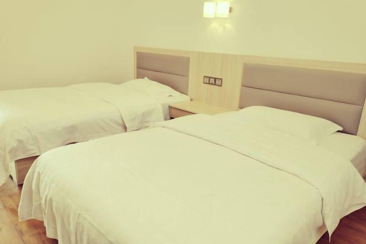A hotel room with two beds, a wooden headboard, a nightstand, and a wall-mounted light fixture.