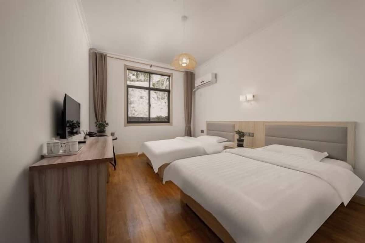 A hotel room with two beds, a desk, a television, and a window with curtains.