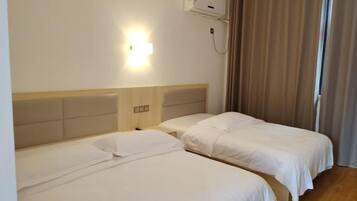 Quarto de hotel com duas camas de solteiro, uma mesa de cabeceira, ar condicionado fixado na parede e uma janela com cortinas.