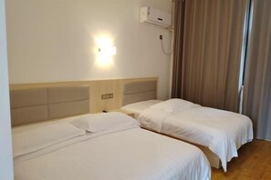 Une chambre d’hôtel avec deux lits simples, une table de chevet, un climatiseur fixé au mur et une fenêtre avec des rideaux.
